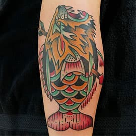 Traditionele tattoo van een vis met een pijl erdoorheen op het onderbeen.