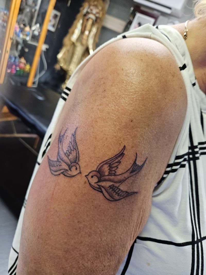 Twee kleine zwaluwen in fineline stijl op de bovenarm.