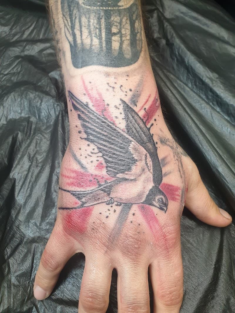 Zwaluw tattoo op hand met rode en zwarte inkt spetters.