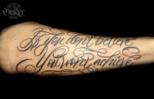 Grote script tattoo op onderarm met tekst 'If you don't believe you won't achieve'.