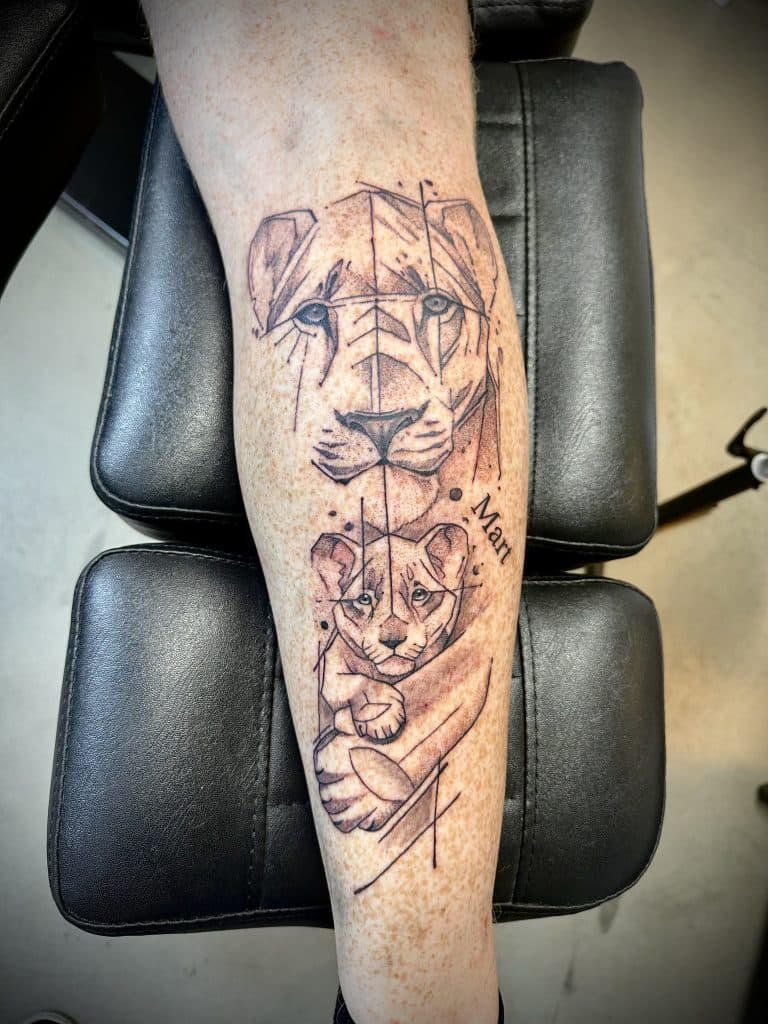 Geometrische leeuwin en welp tattoo op onderbeen met naam 'Mart'.