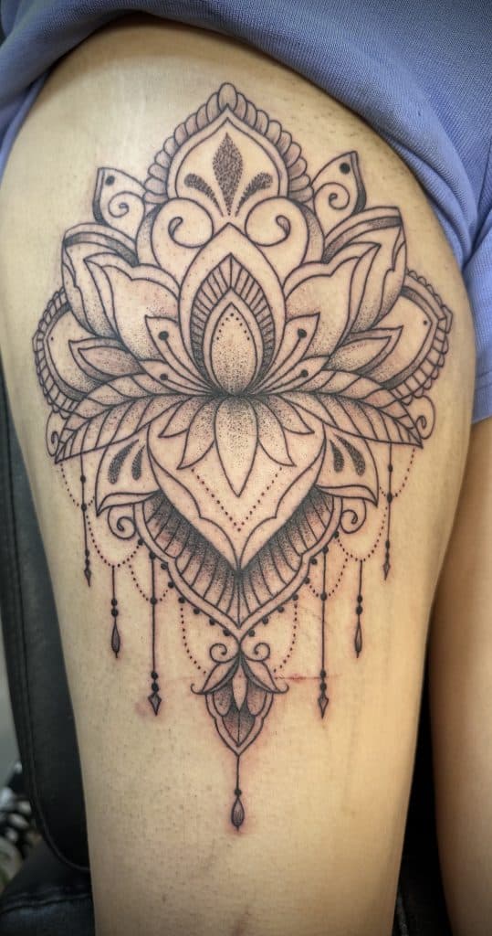Mandala lotusbloem met dotwork en hangende ornamenten op bovenbeen.