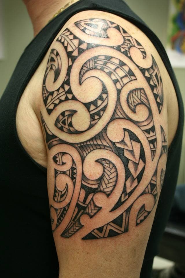 Grote zwarte tribale tattoo met koru patronen op de bovenarm.