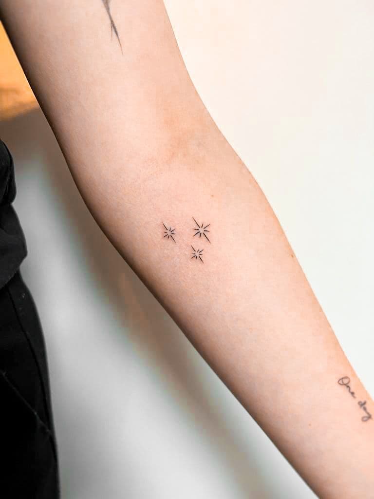 Minimalistische fineline tattoo van drie sterretjes op de bovenarm.