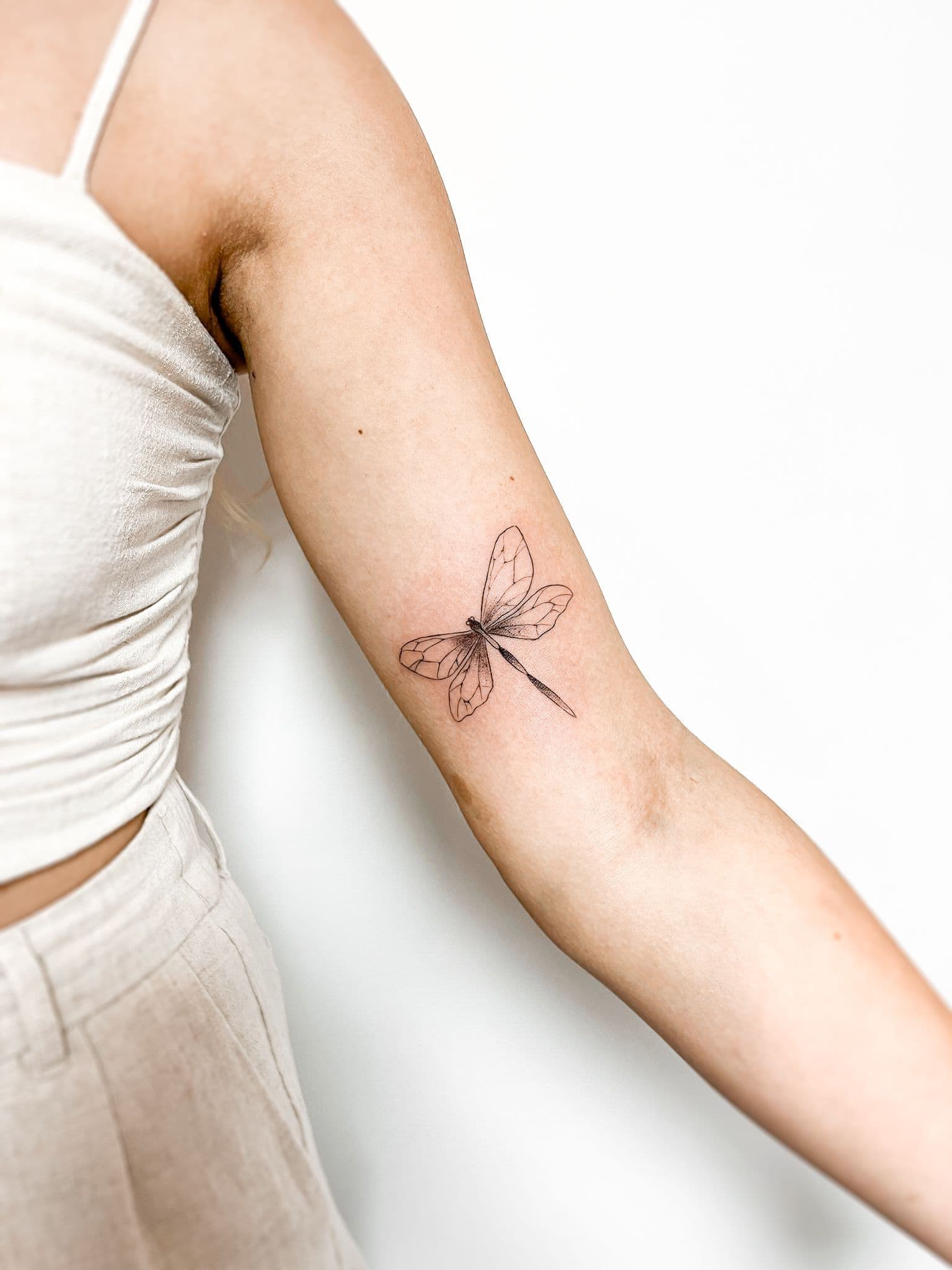 Fineline libelle tattoo op de binnenkant van de bovenarm.