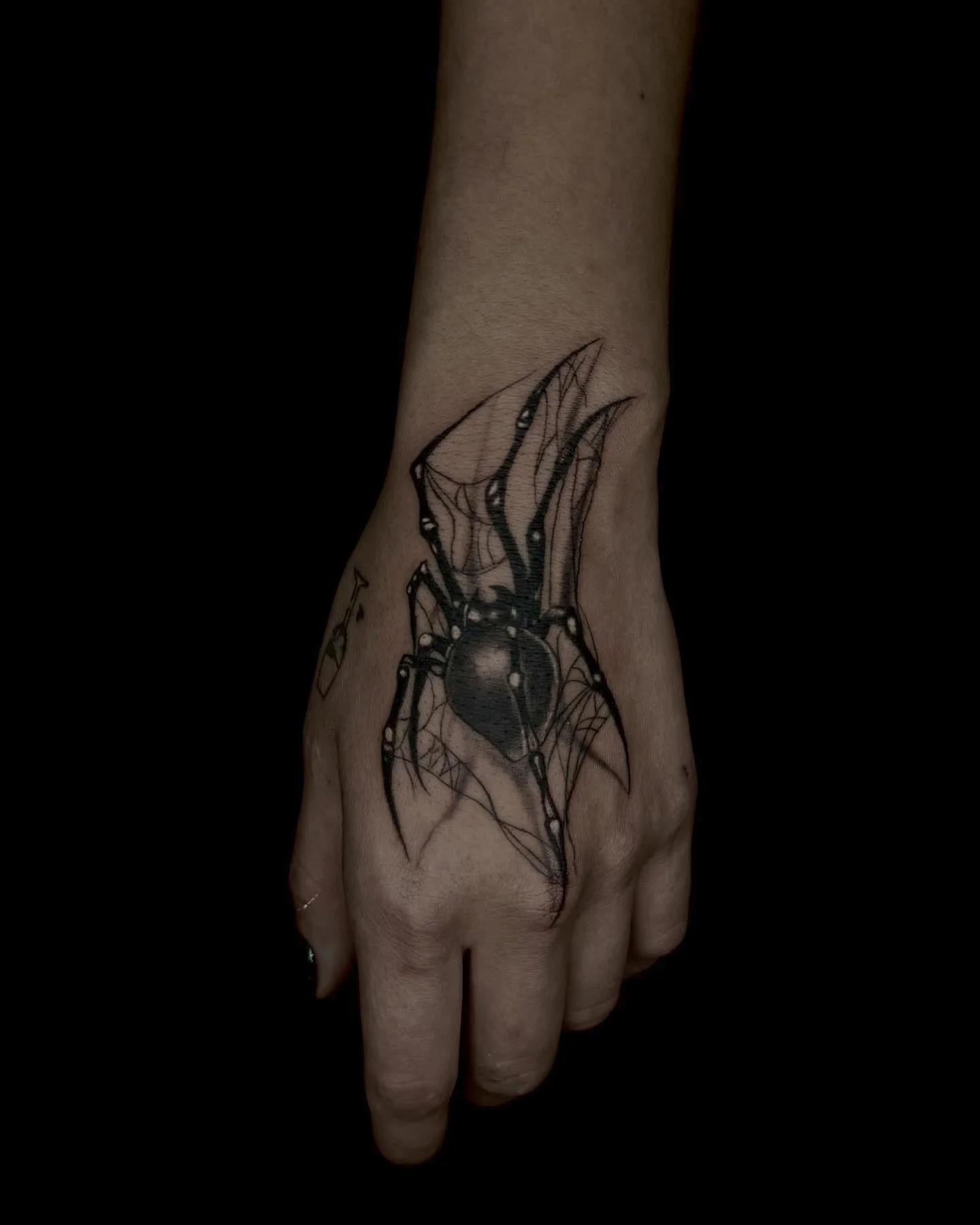 Zwart-witte spin in web tattoo op de bovenkant van de hand.