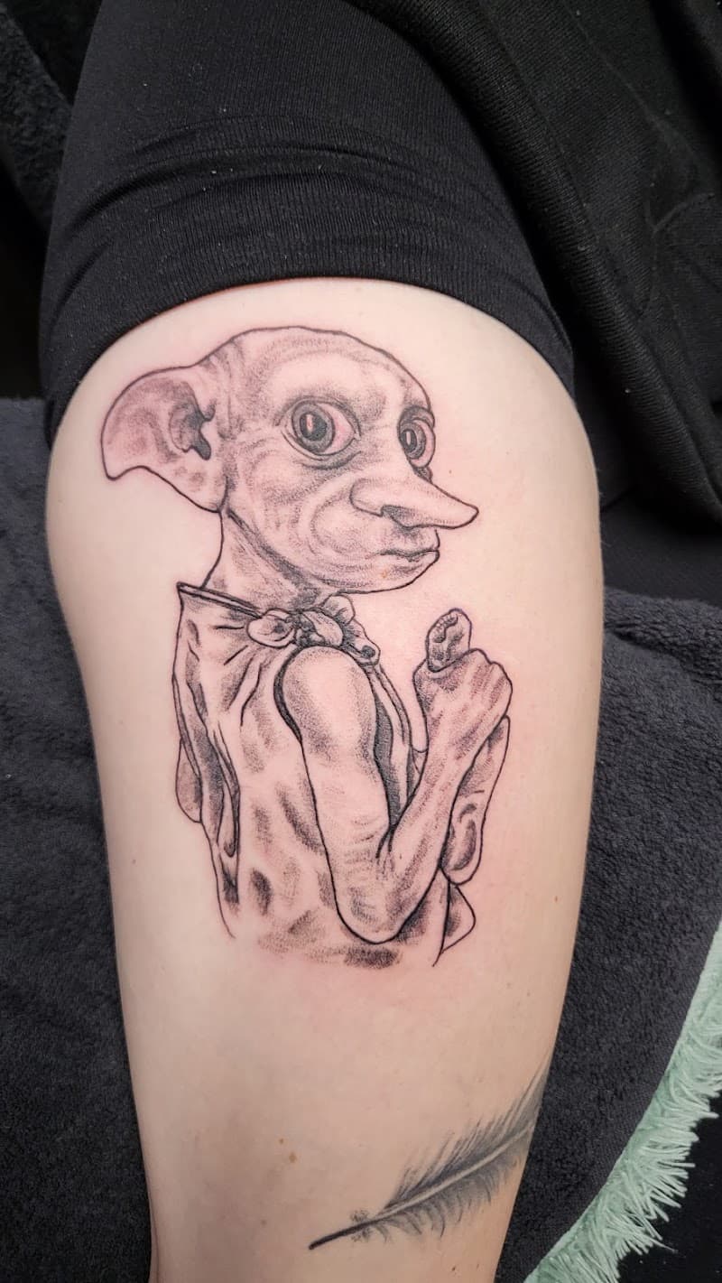 Illustratieve zwart-wit tattoo van Dobby de huiself op het bovenbeen.