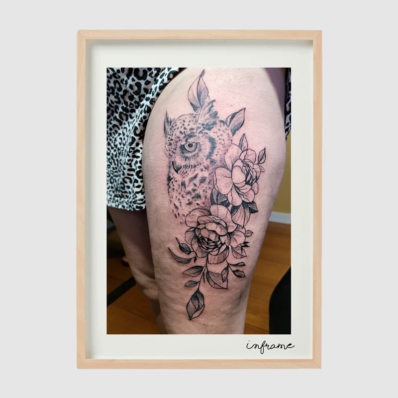 Zwart-wit tattoo van een uil met bloemen op het bovenbeen.