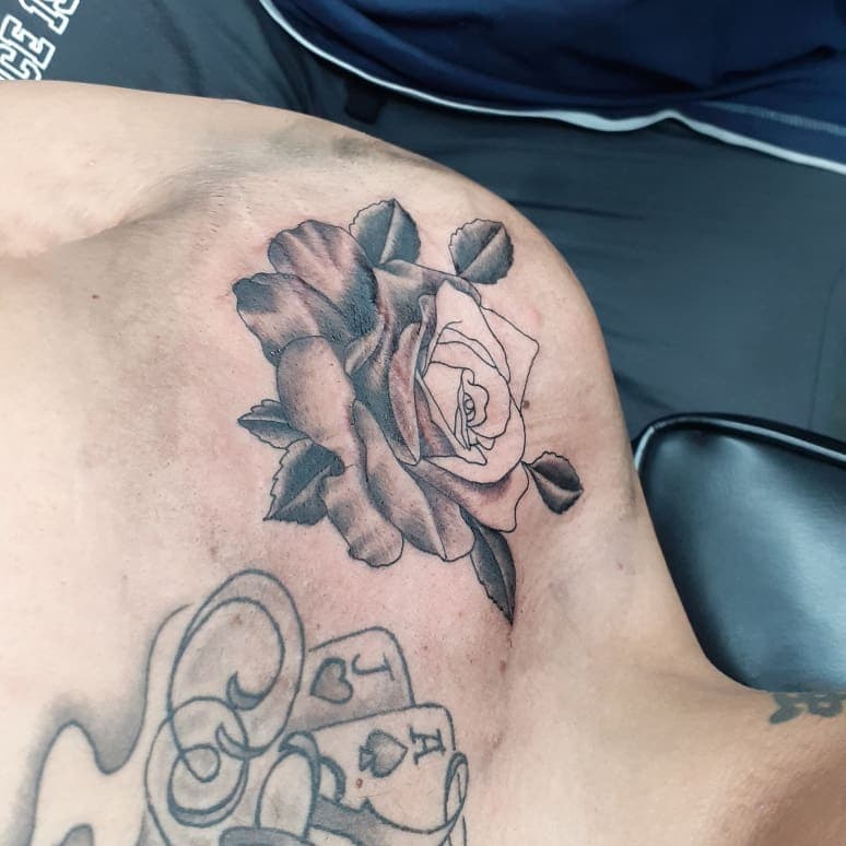Zwart-wit roos en speelkaarten tattoo op borst.