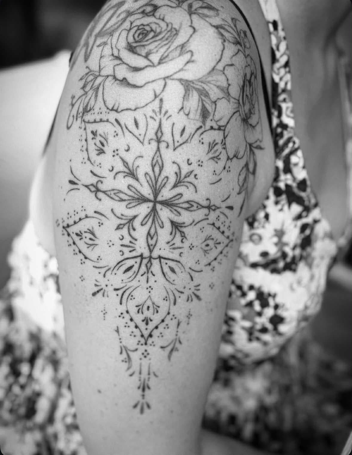 Fineline ornamental tattoo met roos op bovenarm.