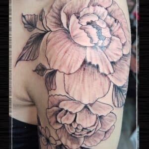 Grote zwart-wit pioenroos tattoo op de bovenarm.