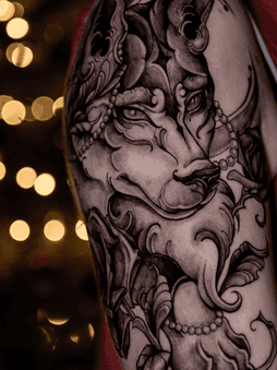 Gedetailleerde wolf tattoo met sierlijke elementen en parels op bovenarm.