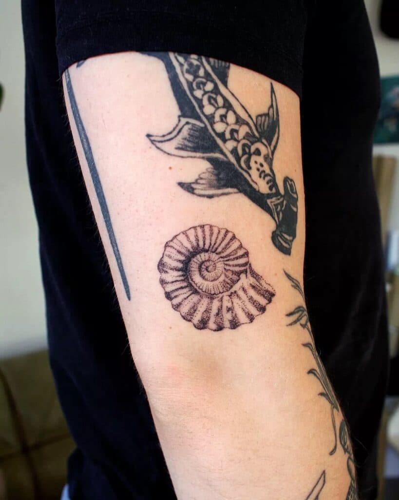 Zwart-wit ammoniet fossiel en dolk op bovenarm.