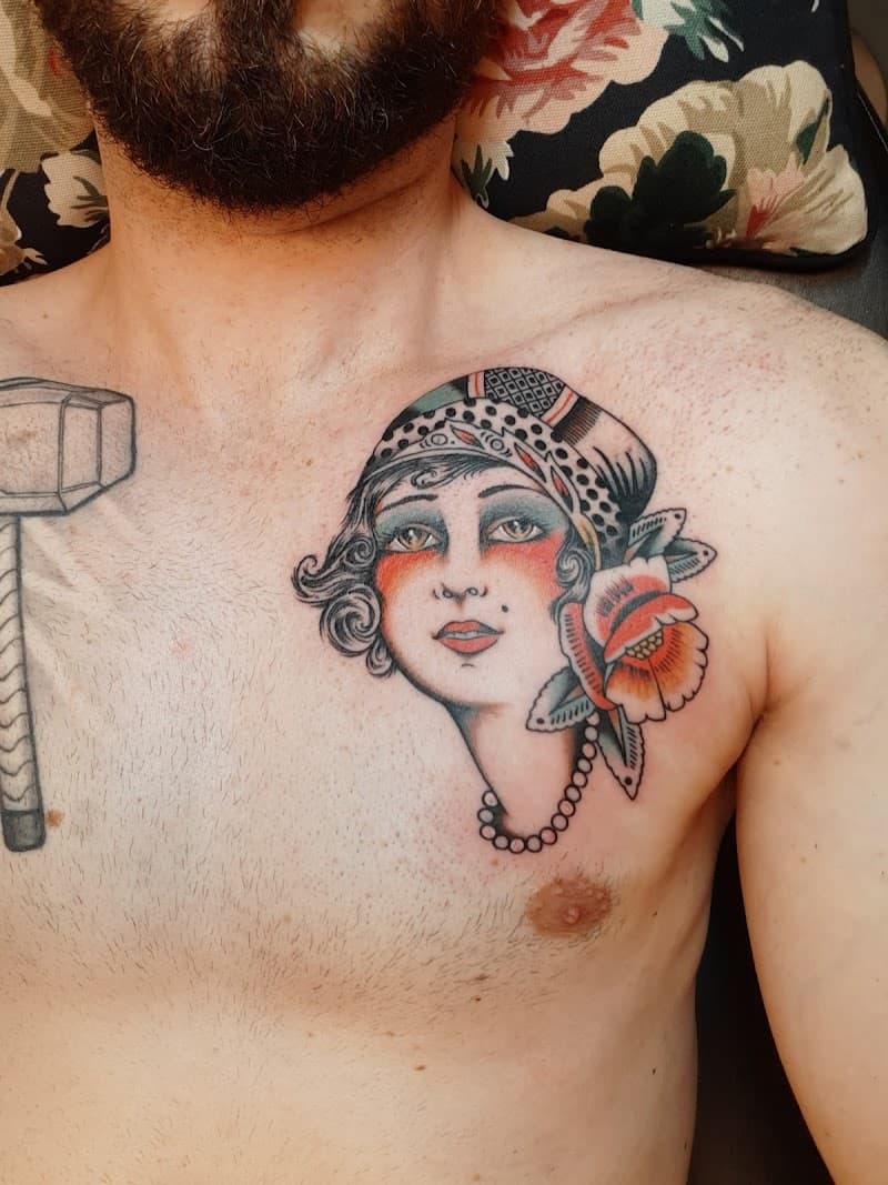 Traditionele tattoo van een vrouwenhoofd met hoofddoek en bloem op de borst.