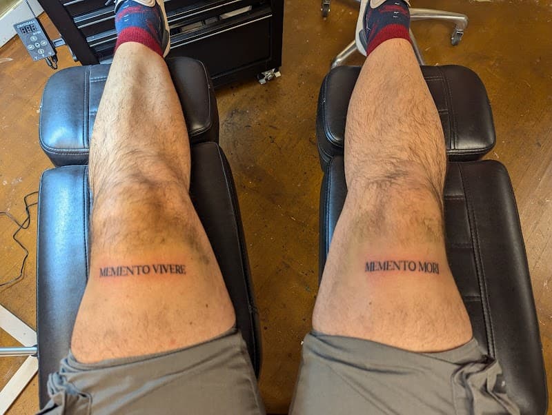 Memento Vivere en Memento Mori tekst tattoos op beide bovenbenen.
