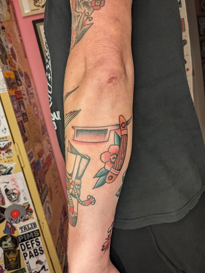 Traditionele tattoo van een open scheermes en een bloem op de onderarm.