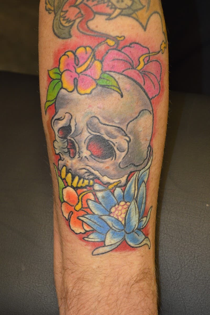 Neo-traditionele schedel met hibiscus en lotus bloemen op onderbeen.