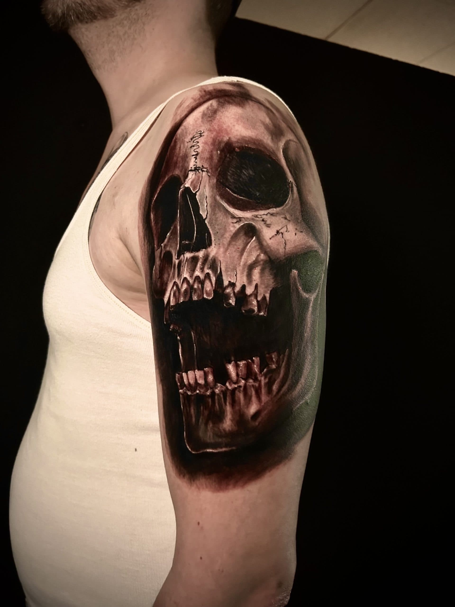 Grote realistische schedel tattoo met open mond op de bovenarm.