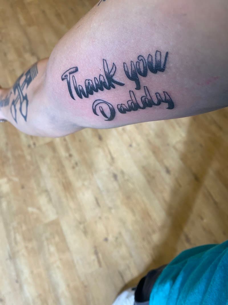 "Thank you Daddy" tekst tattoo in sierlijk lettertype op de bovenarm.
