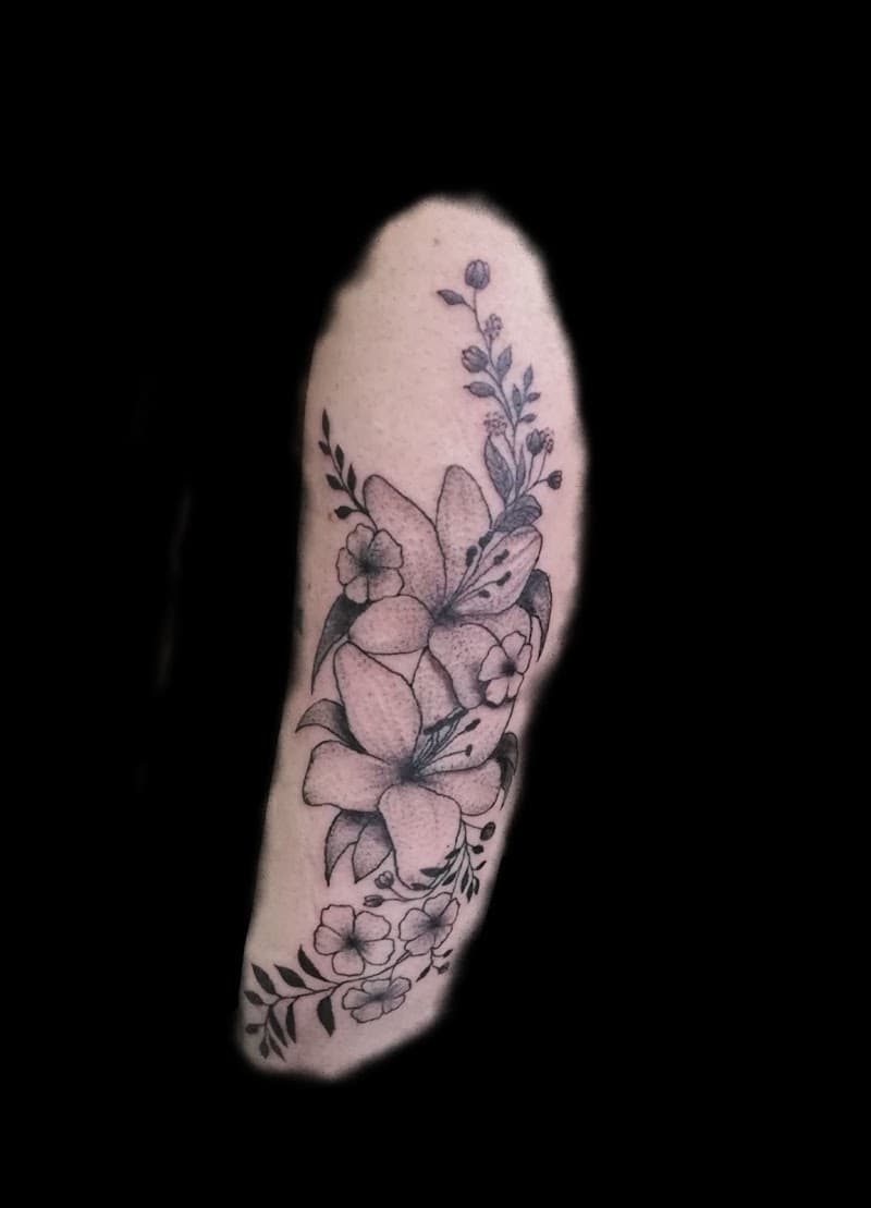 Zwart-wit bloemen tattoo met lelies en bladeren op de bovenarm.