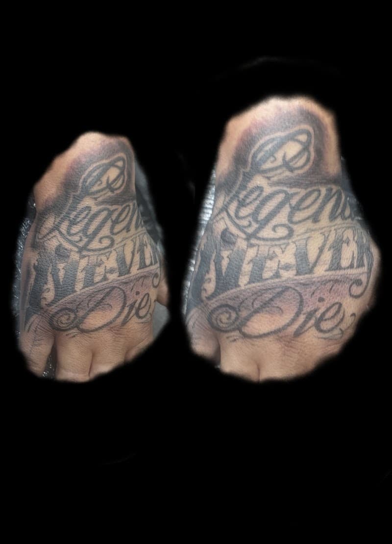 Zwart-wit 'Legends Never Die' tekst tattoo op de hand.