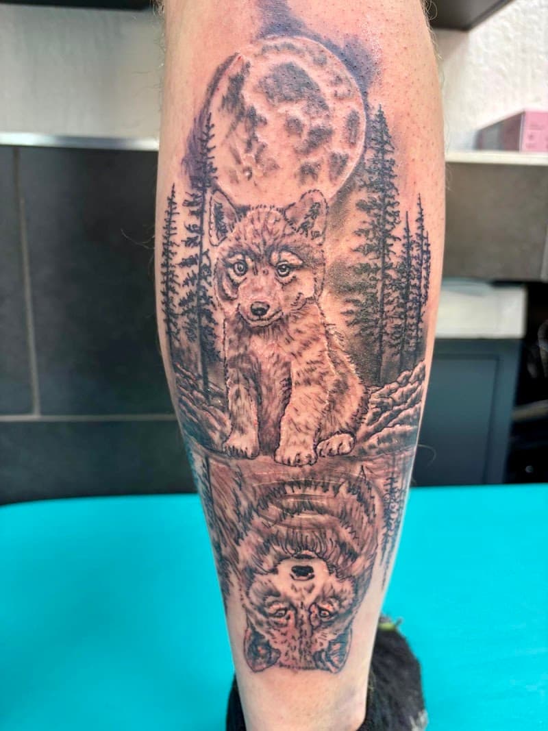 Realistische tattoo van wolf welp met reflectie van volwassen wolf, maan en bos.