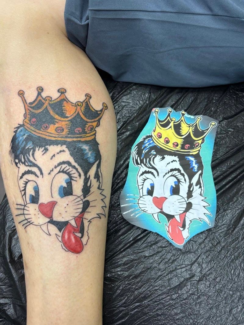 Traditional tattoo van een kattenkop met een kroon en tong uit.