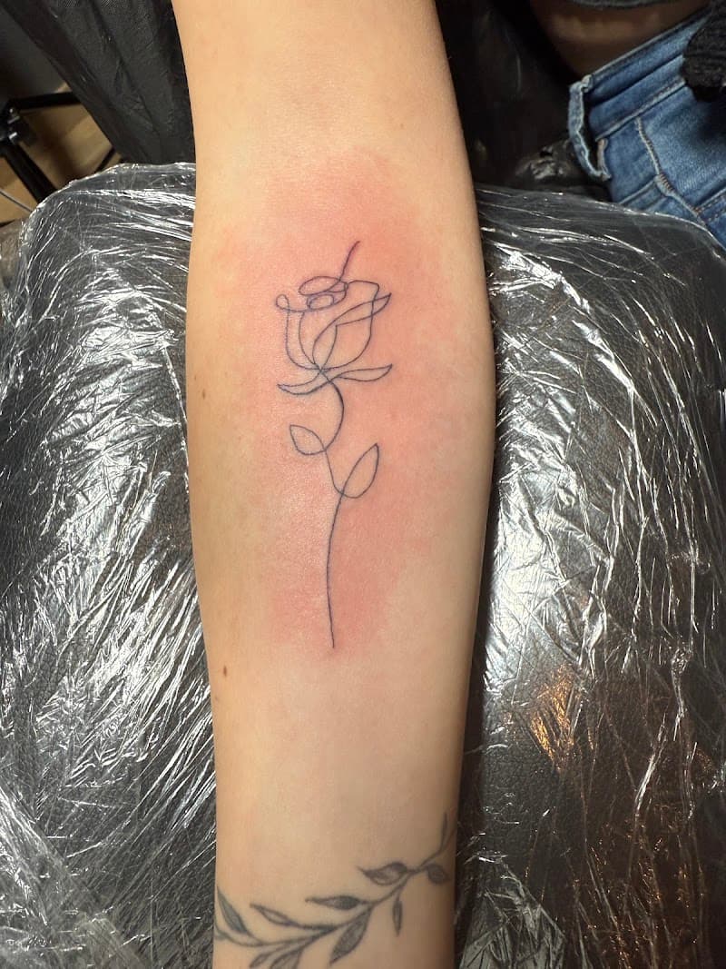 Minimalistische fineline roos tattoo op onderarm.