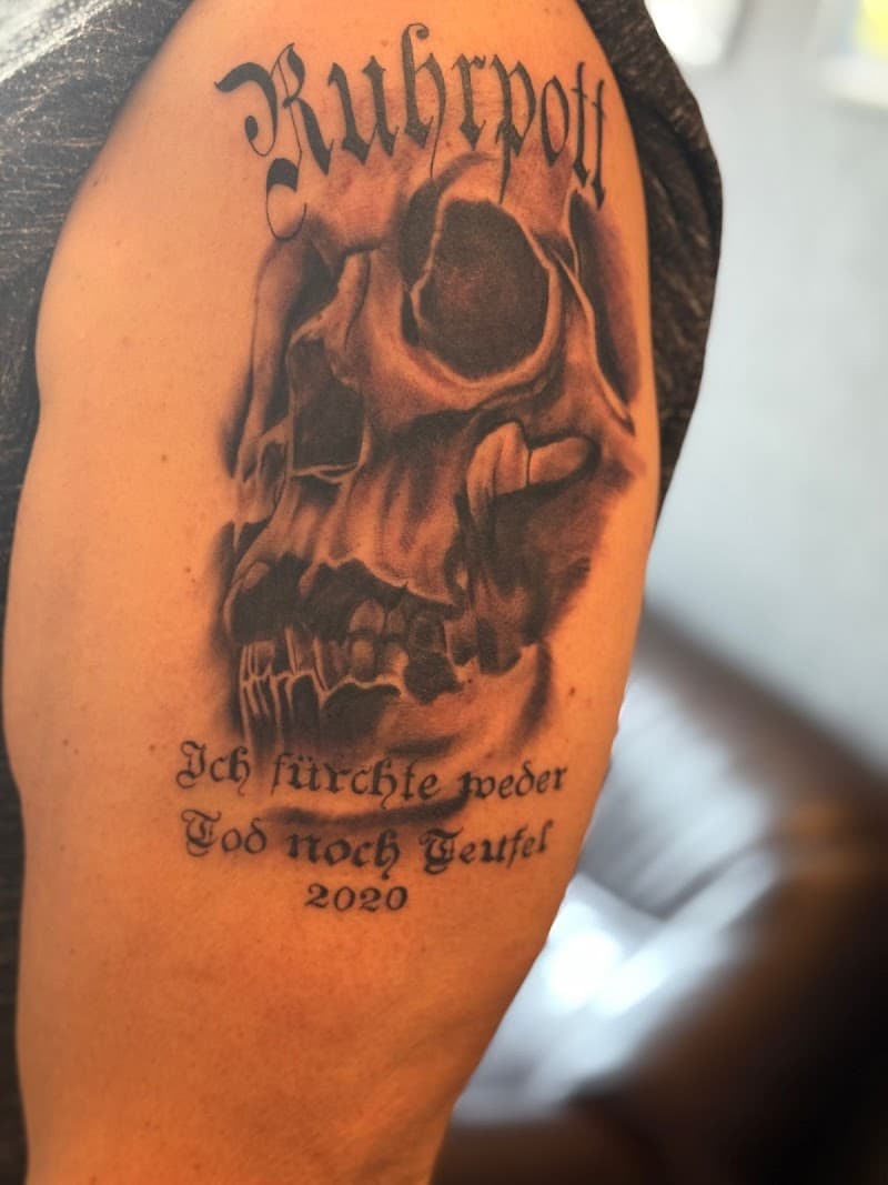 Zwart-wit schedel met "Ruhrpott" en Duitse tekst op bovenarm.