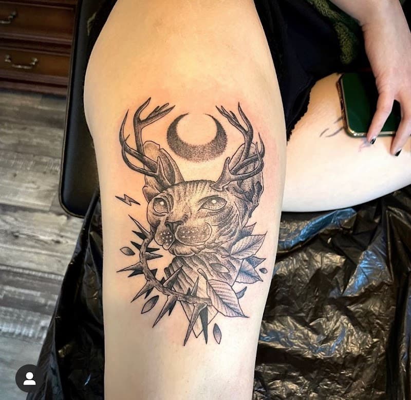 Zwart-wit tattoo van een Sphynx kat met gewei, maan en doornen op het bovenbeen.