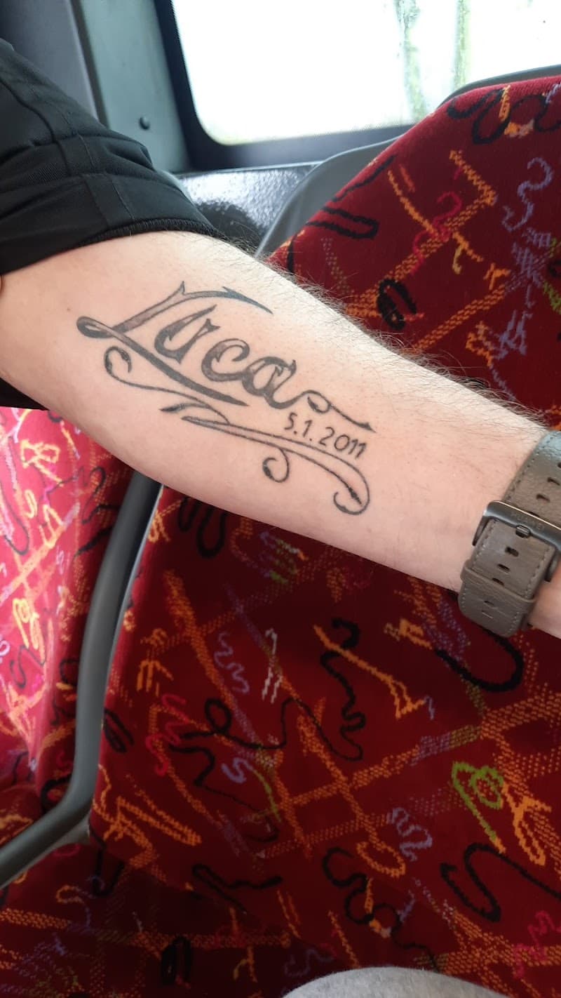 Sierlijke lettering tattoo van de naam 'Luca' en datum '5.1.2011' op de onderarm.