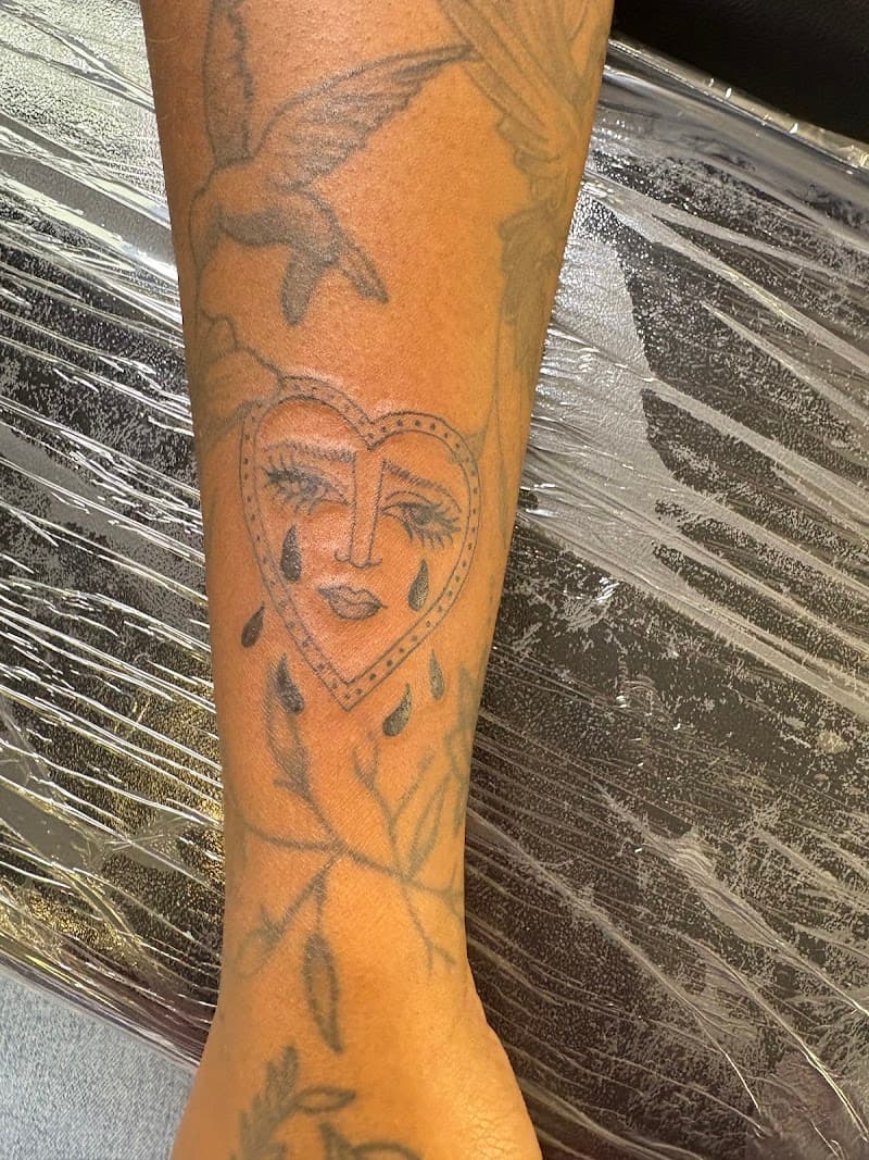 Fineline tattoo van een hart met een huilend gezicht erin op het onderbeen.