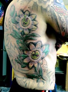 Grote passiebloem tattoo op de ribben, deels ingekleurd.