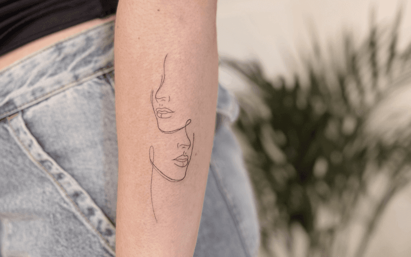 Fineline tattoo van twee gezichten in één lijn op de onderarm.