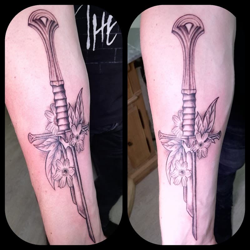 Blackwork zwaard met bloemen en bladeren op onderarm.