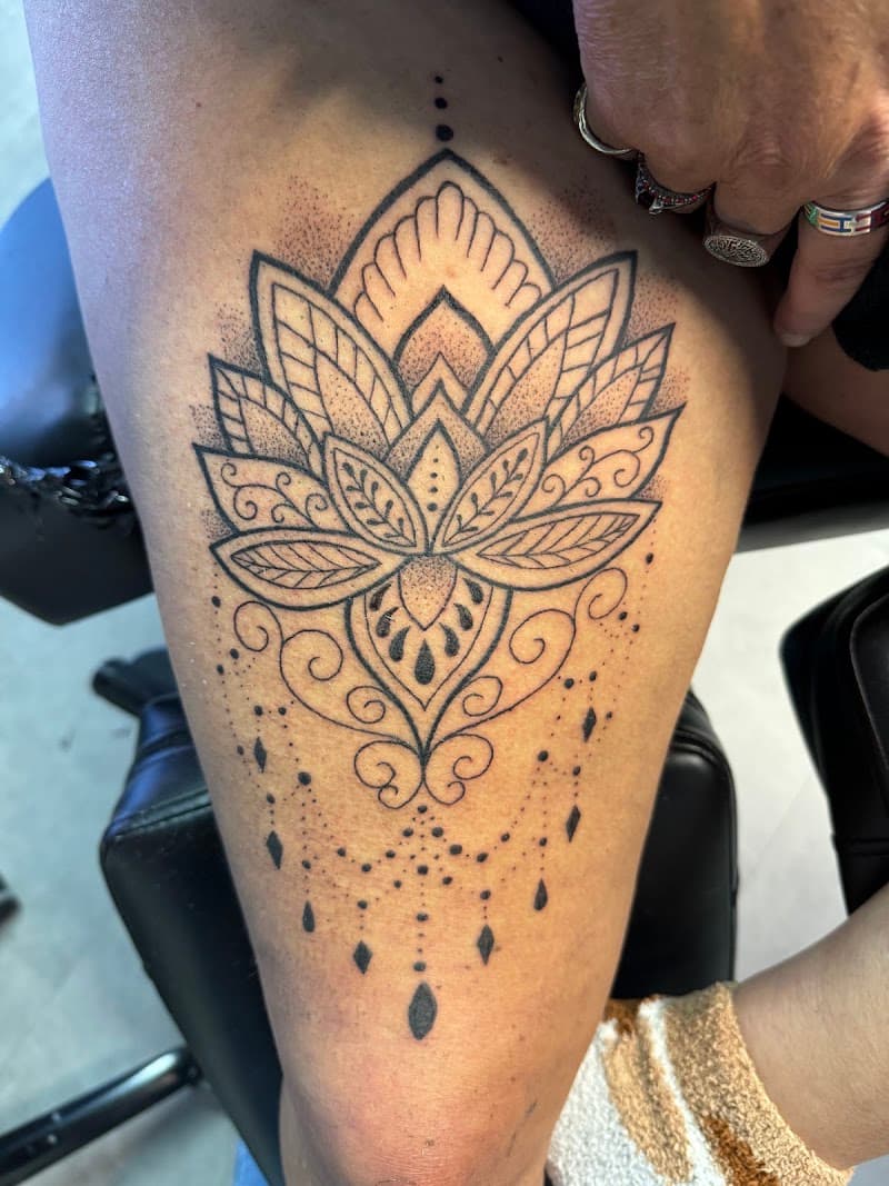 Zwartwerk lotusbloem met ornamenten en dotwork druppels op bovenbeen.