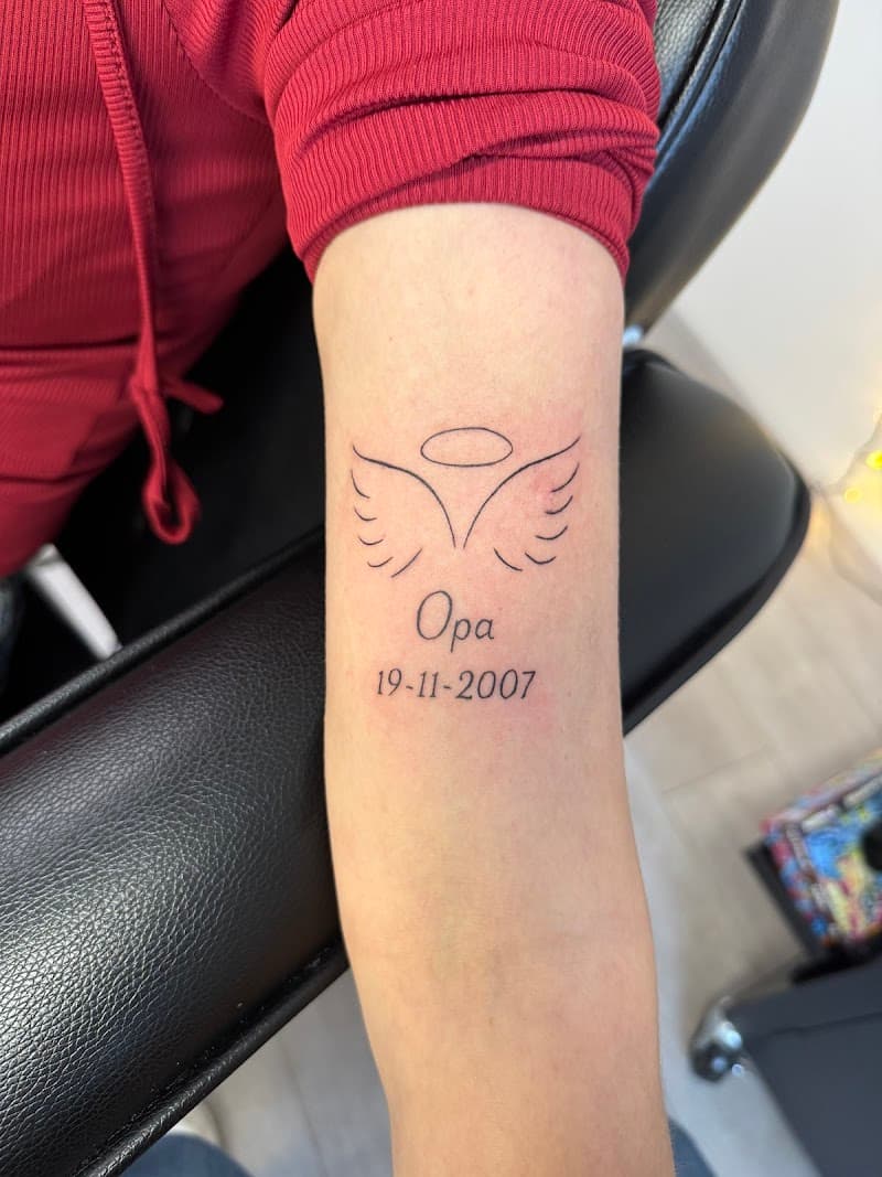 Fineline herdenkingstattoo met vleugels, halo, 'Opa' en datum.
