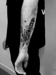 Zwart-wit traditionele dolk tattoo op onderarm.