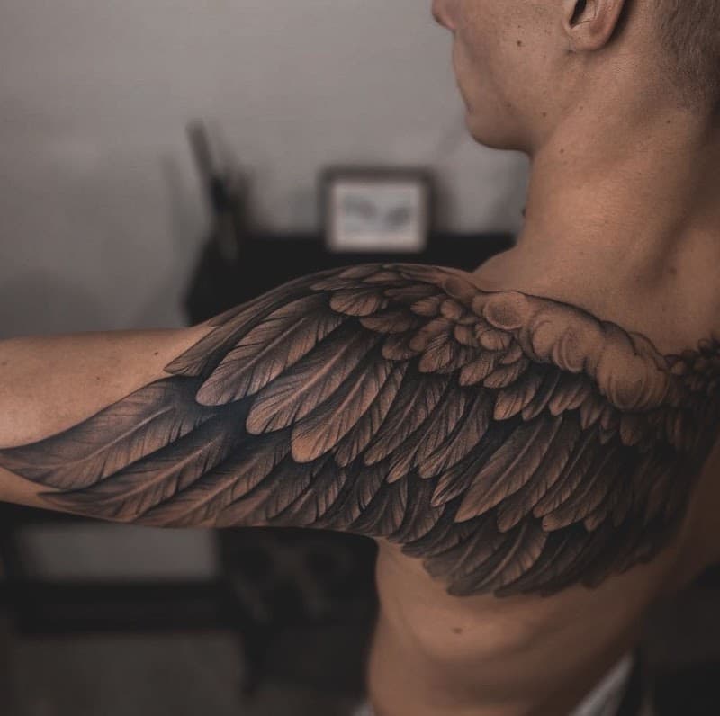 Grote, gedetailleerde vleugel tattoo in zwart-wit op schouder en bovenarm.