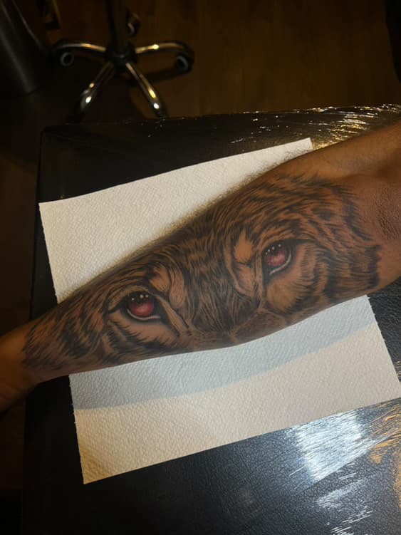 Realistische tijgerogen tattoo met rode ogen op onderarm.