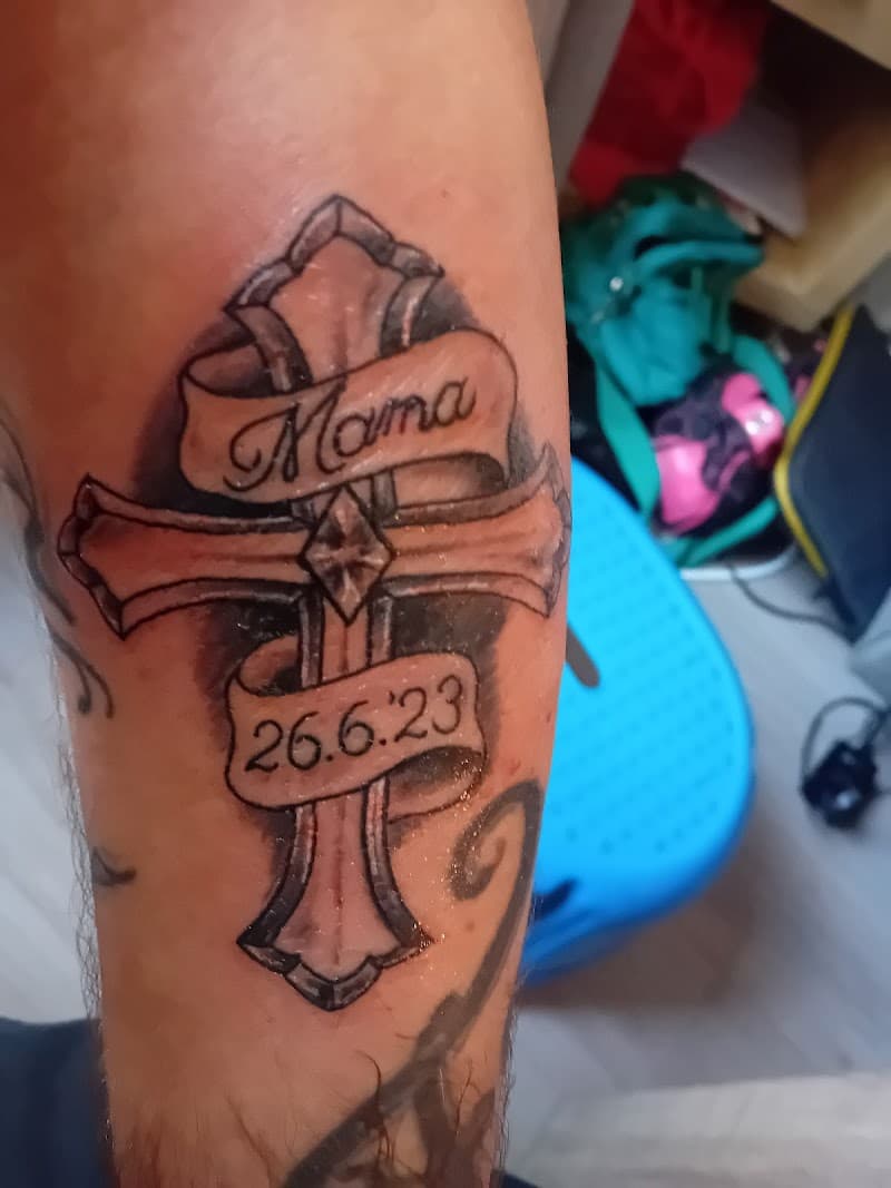 Kruis tattoo met 'Mama' banner en datum 26.6.23 op onderarm.