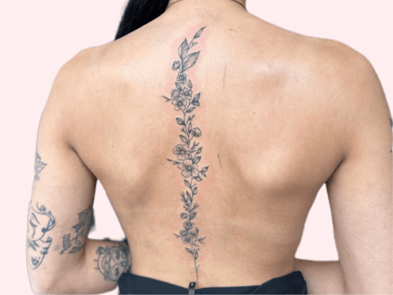 Fineline bloemenrank tattoo langs de ruggengraat.