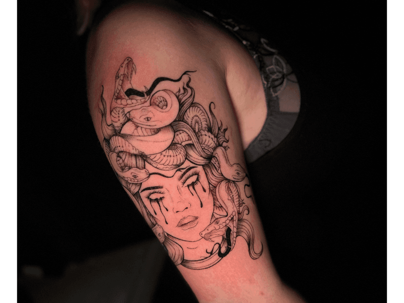 Blackwork Medusa tattoo met slangenhaar en tranen op bovenarm.