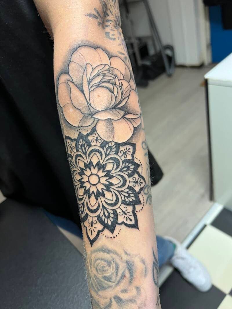 Grote bloem en mandala tattoo op onderarm in blackwork stijl.