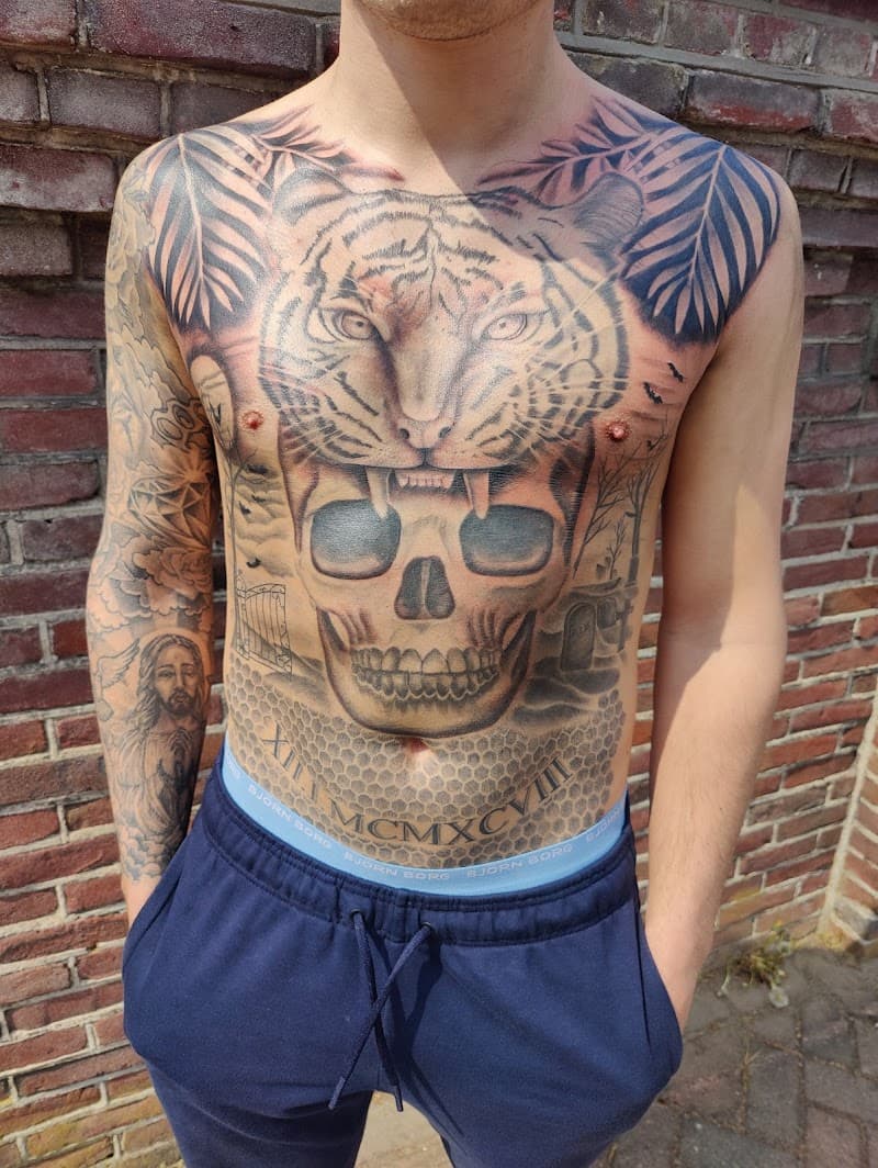 Grote borsttattoo van een tijgerkop boven een schedel, met bladeren en een kerkhof.