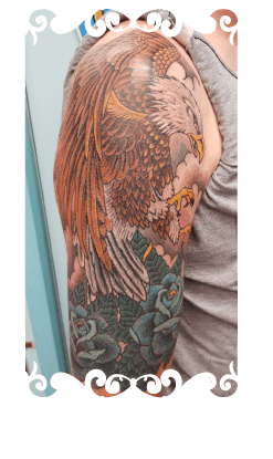 Traditionele tattoo van een adelaar en blauwe rozen op de bovenarm.