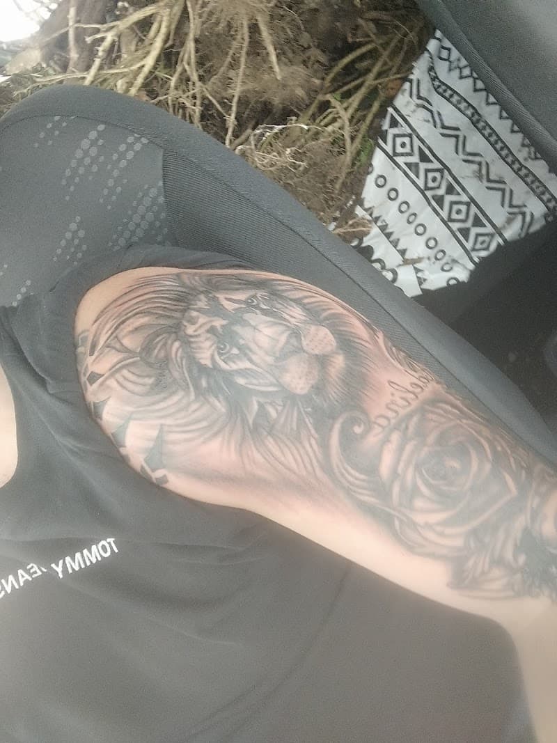 Zwart-grijze tattoo van een leeuwenkop en een roos op de bovenarm.