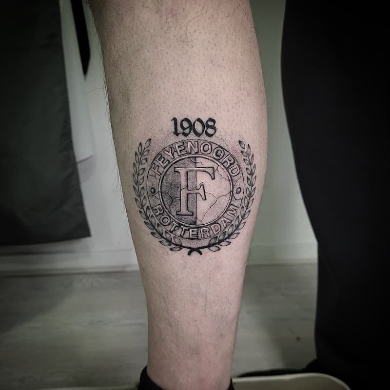 Feyenoord Rotterdam logo met 1908 en stenen textuur op onderbeen.