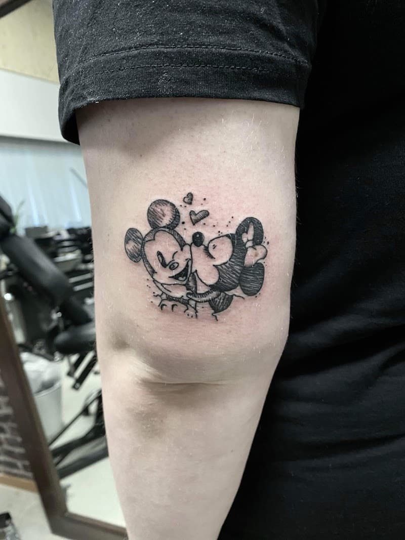 Schetsstijl tattoo van kussende Mickey en Minnie Mouse met hartjes op bovenarm.