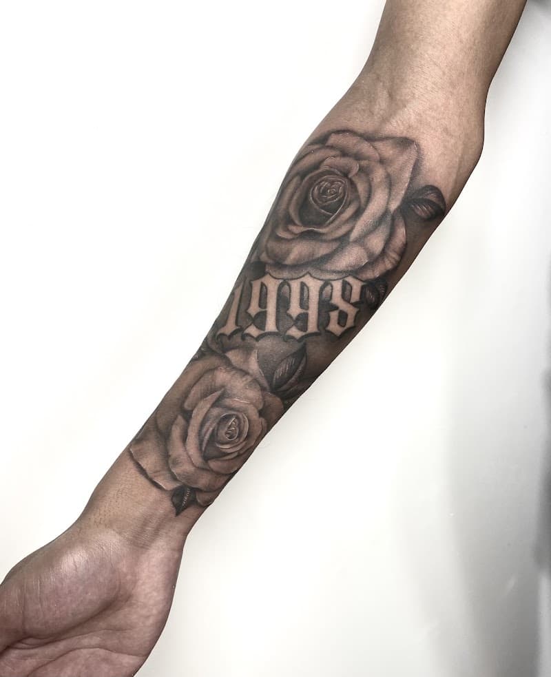 Zwart-grijze tattoo van twee rozen en het jaartal 1998 op de onderarm.
